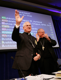 PASSING THE MANTLE Archbishop Joseph E. Kurtz of Louisville acknowledges applause by fellow bishops following his election Nov. 12 as president of the U.S. Conference of Catholic Bishops. Outgoing USCCB President Cardinal Timothy Dolan of New York is shown with Archbishop Kurtz. Catholic News Service