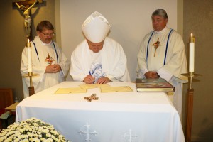 Bishop Richard F. Stika signs the decree formally establishing Blessed Teresa of Calcutta Parish during a special Mass Sept. 5. Observing are Deacon Sean Smith, diocesan chancellor, and Father Steve Pawelk, pastor of the new parish. Photo by Bill Brewer