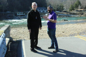 Father Tom Charters, GHM, left, and Brother Corey Soignier, GHM, of St. Michael the Archangel Parish in Erwin, in March stand at the edge of a road and bridge that was washed away by the rain-swollen Nolichucky River in Unicoi County in September. (Photo Dan McWilliams)